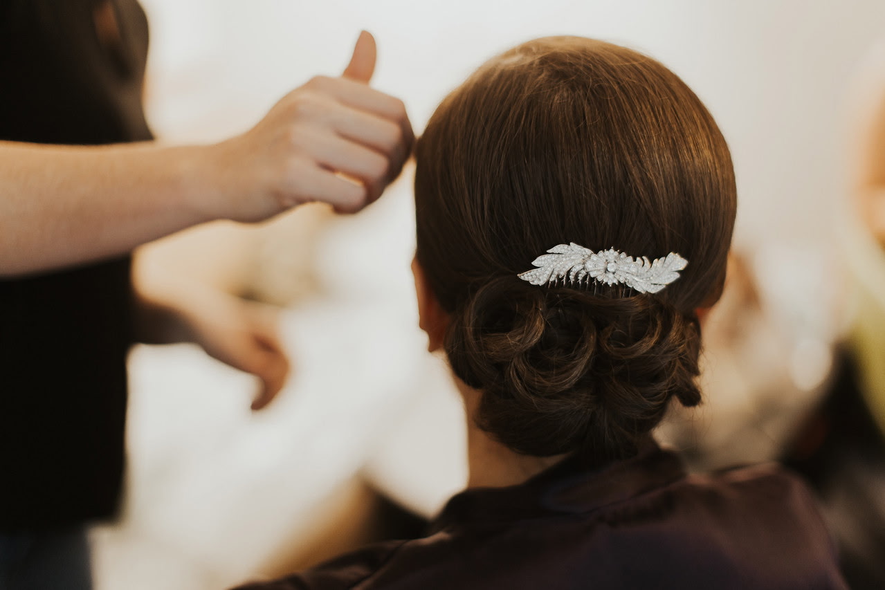 Close-up of a detailed bridal updo with a decorative hairpiece as the stylist finishes the hairstyle